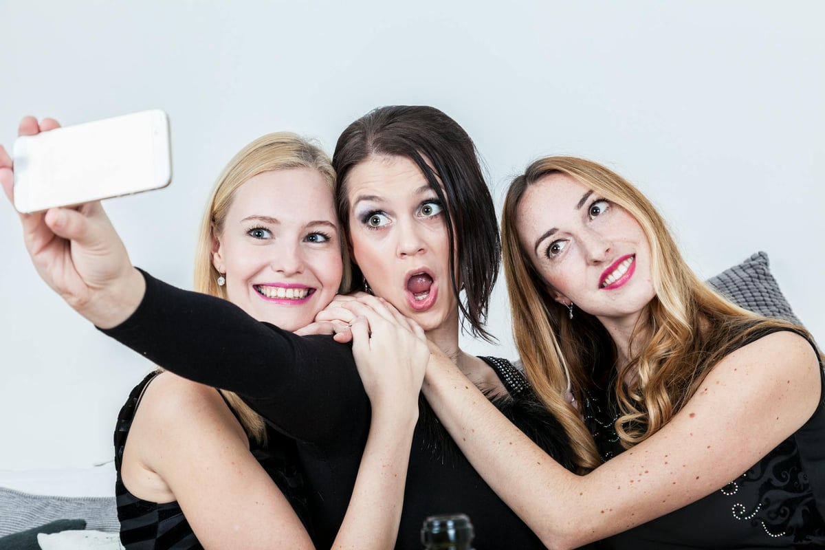 Three joyful women capturing a selfie together, expressing fun and friendship indoors.