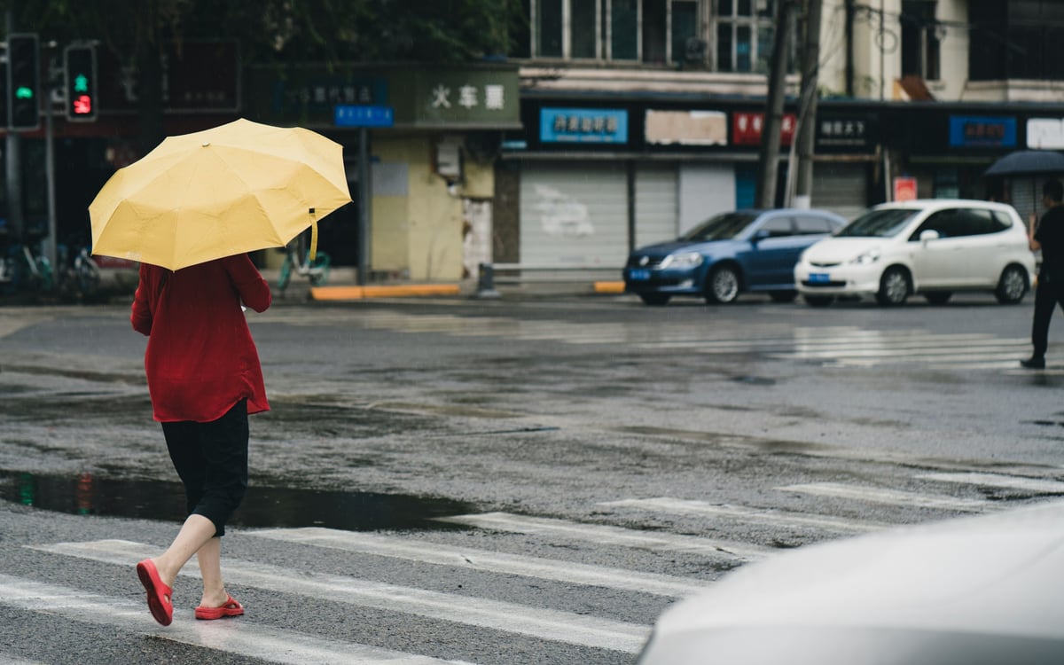 woman in red coat holding yellow umbrella walking on street during daytime