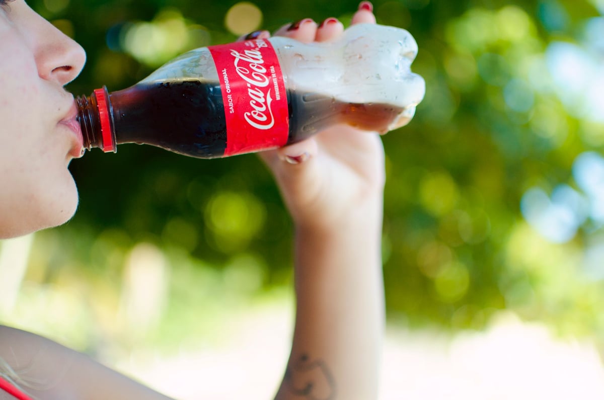 A refreshing moment as a woman drinks a cold bottle of Coca Cola outdoors on a sunny day.