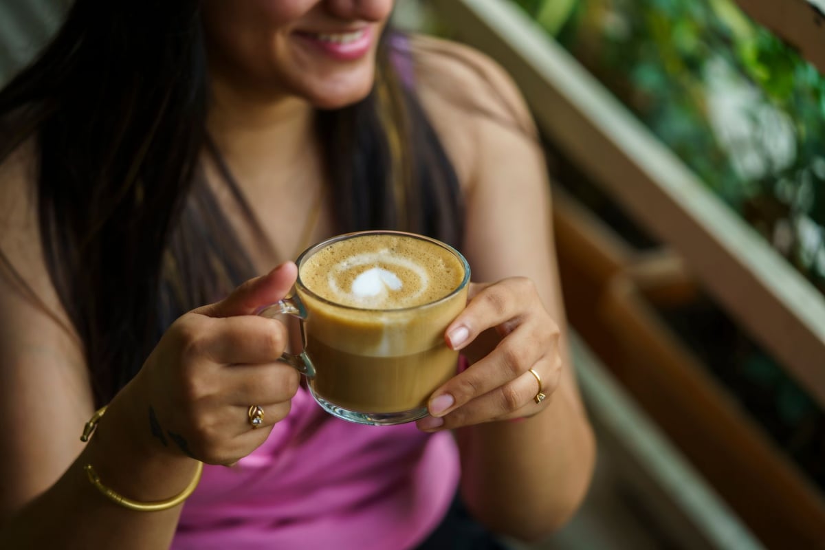 A woman holding a frothy cappuccino in a relaxing setting, sipping coffee.