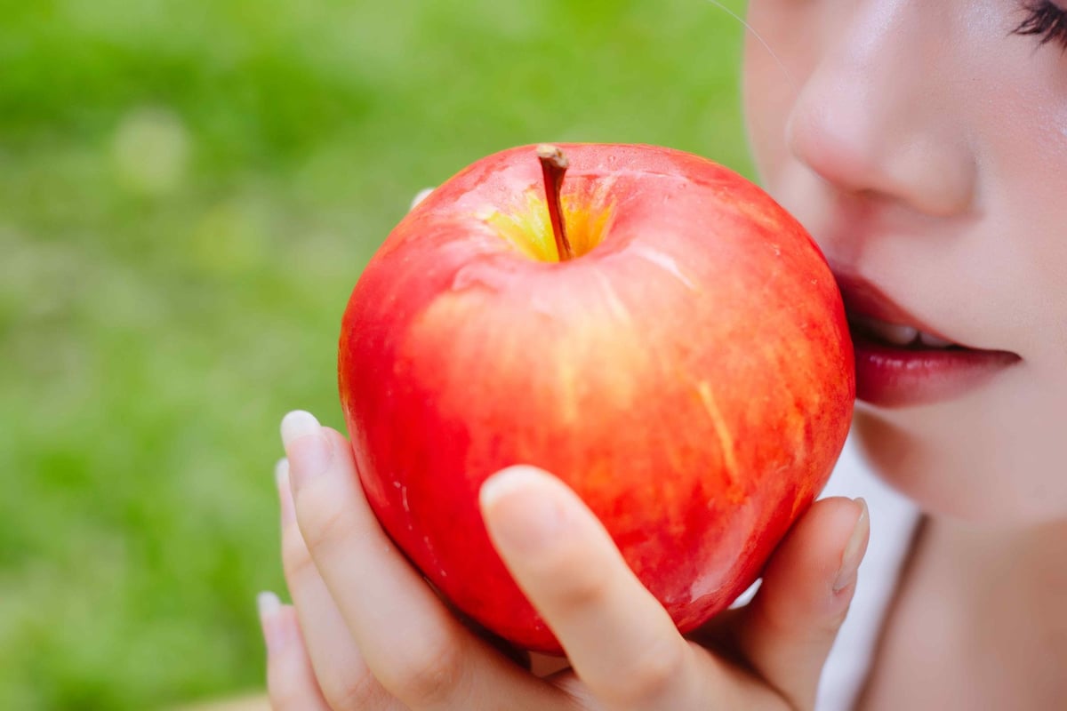 Close-up of a woman holding a bright red apple outdoors, highlighting healthy living and freshness.